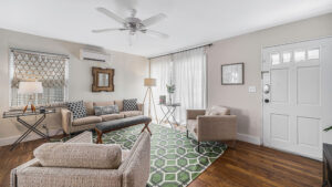 Angled shot of hardwood floor living room with green rug and brown furniture.